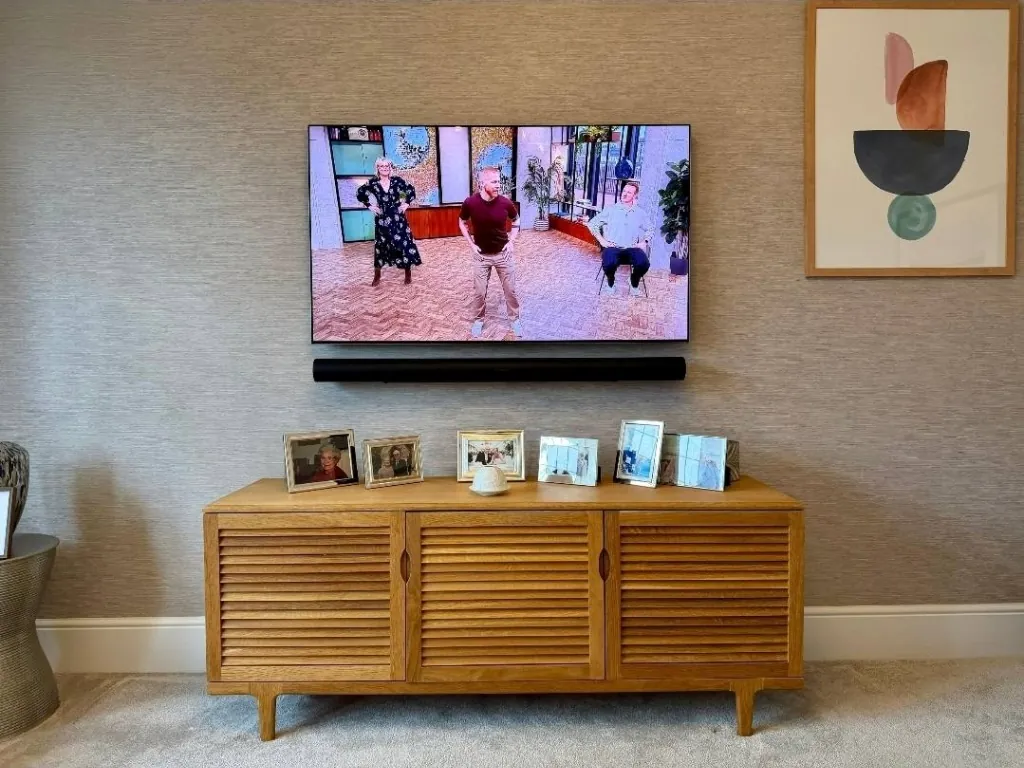 Wall-mounted television above a wooden media cabinet with framed photographs